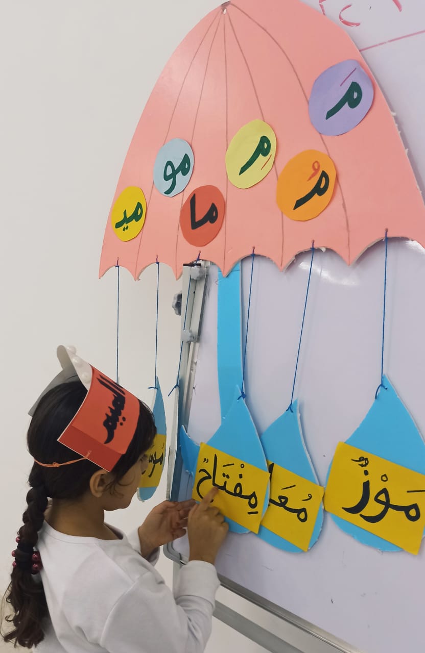 طالبة من الصف الأول تعرض وسيلتها التعليمية على السبورة